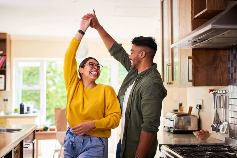 A happy couple dances in their sunlit kitchen